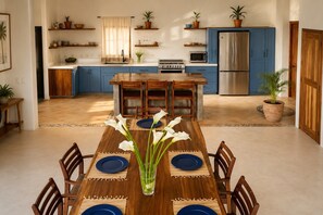 Une cuisine moderne avec des meubles bleus, un îlot central et un coin repas agrémenté d’une table en bois pouvant accueillir six personnes.