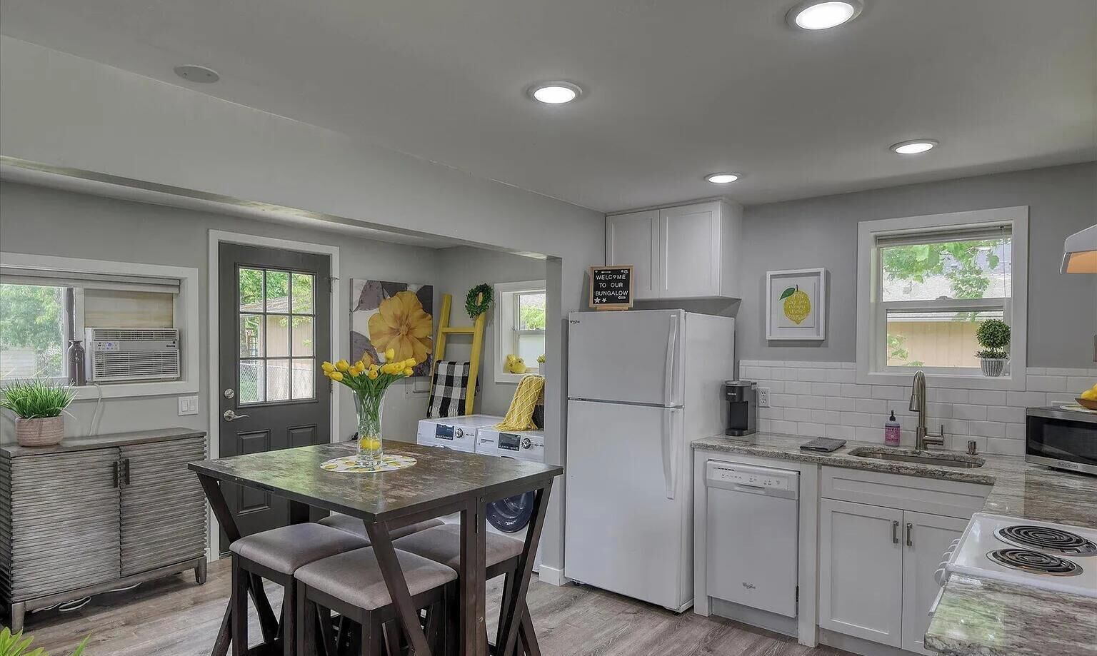 A modern kitchen with white cabinets, a refrigerator, a dishwasher, and a dining area with a table and chairs.