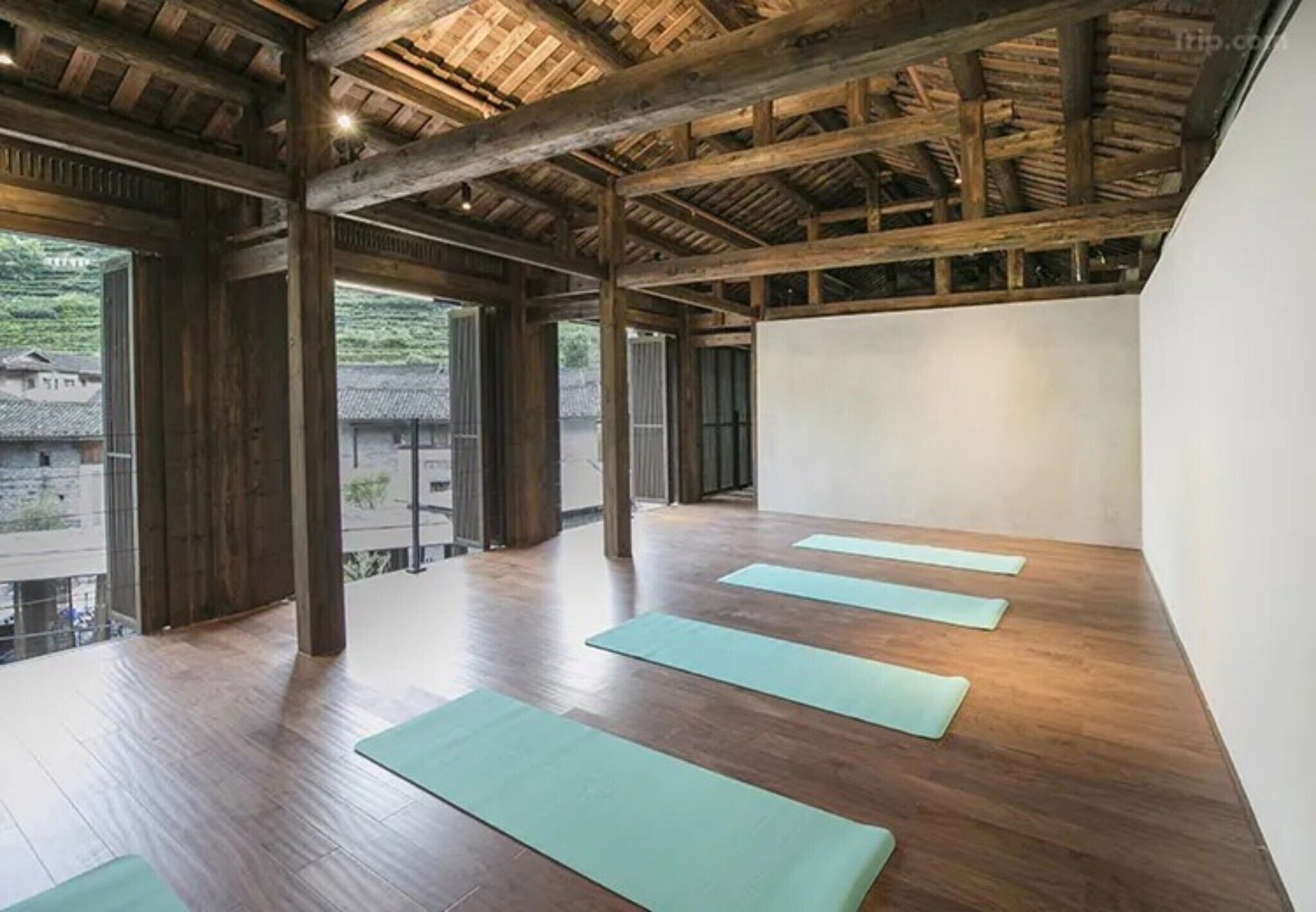 A spacious room with wooden beams and a sloped ceiling, featuring four yoga mats aligned for practice.