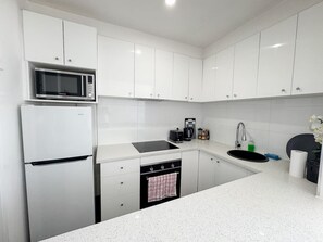 A kitchen with white cabinets, a microwave, a stove, a sink, and a dishwasher. - Clean Bright Studio Apartment - Walkable Location (Saint Kilda East)