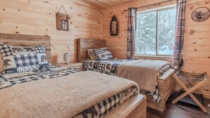 A cabin with two wooden beds, a window with curtains, and a wooden floor.