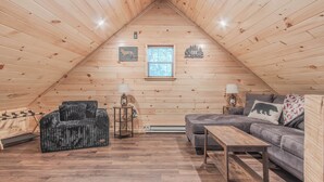 A cozy attic room with wooden walls, a gray sofa, a black chair, and a small table.