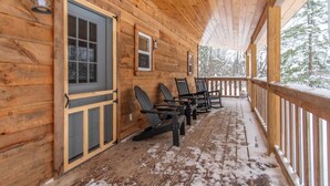 A wooden cabin with a covered porch, wooden chairs, and a door with a window.