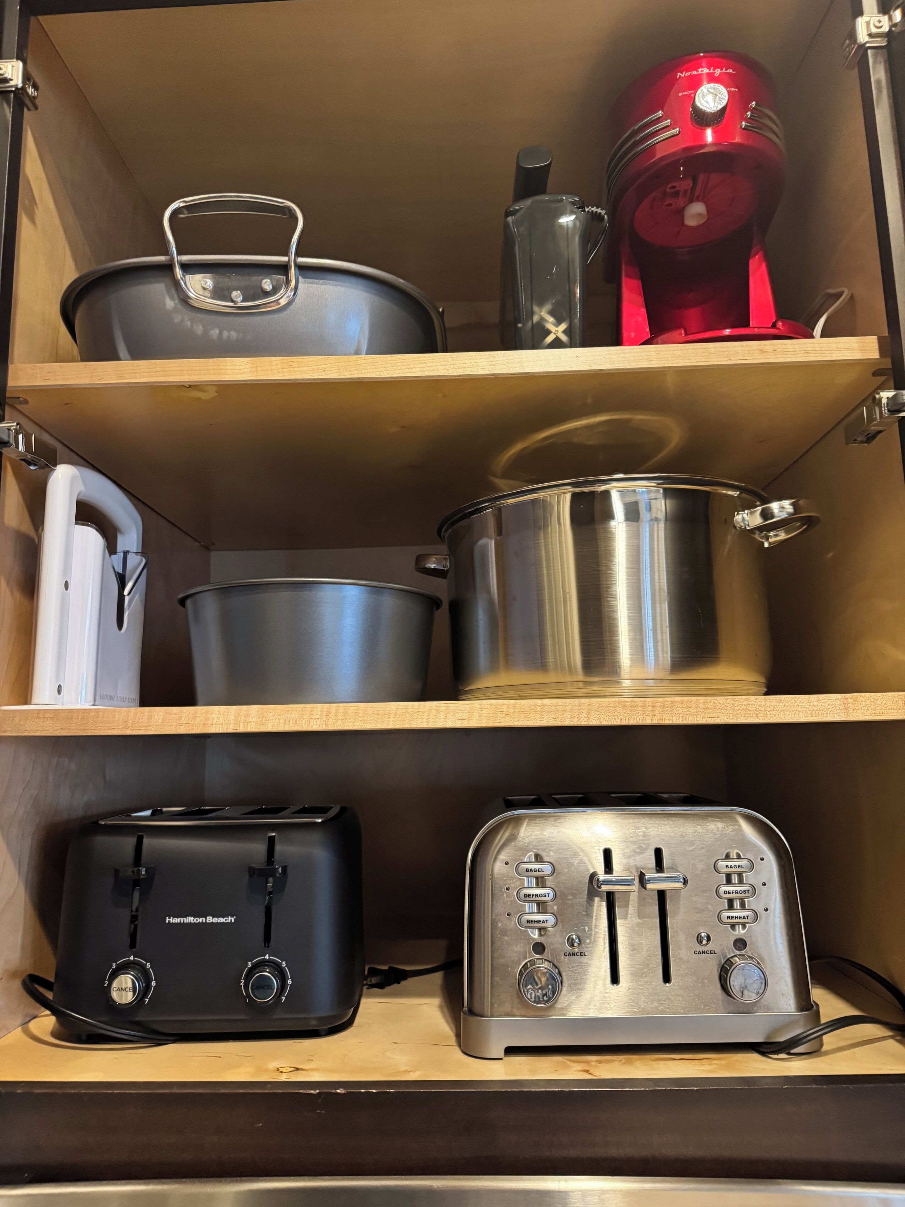 A kitchen with a Hamilton Beach toaster, a silver toaster, and a red appliance on the shelf.