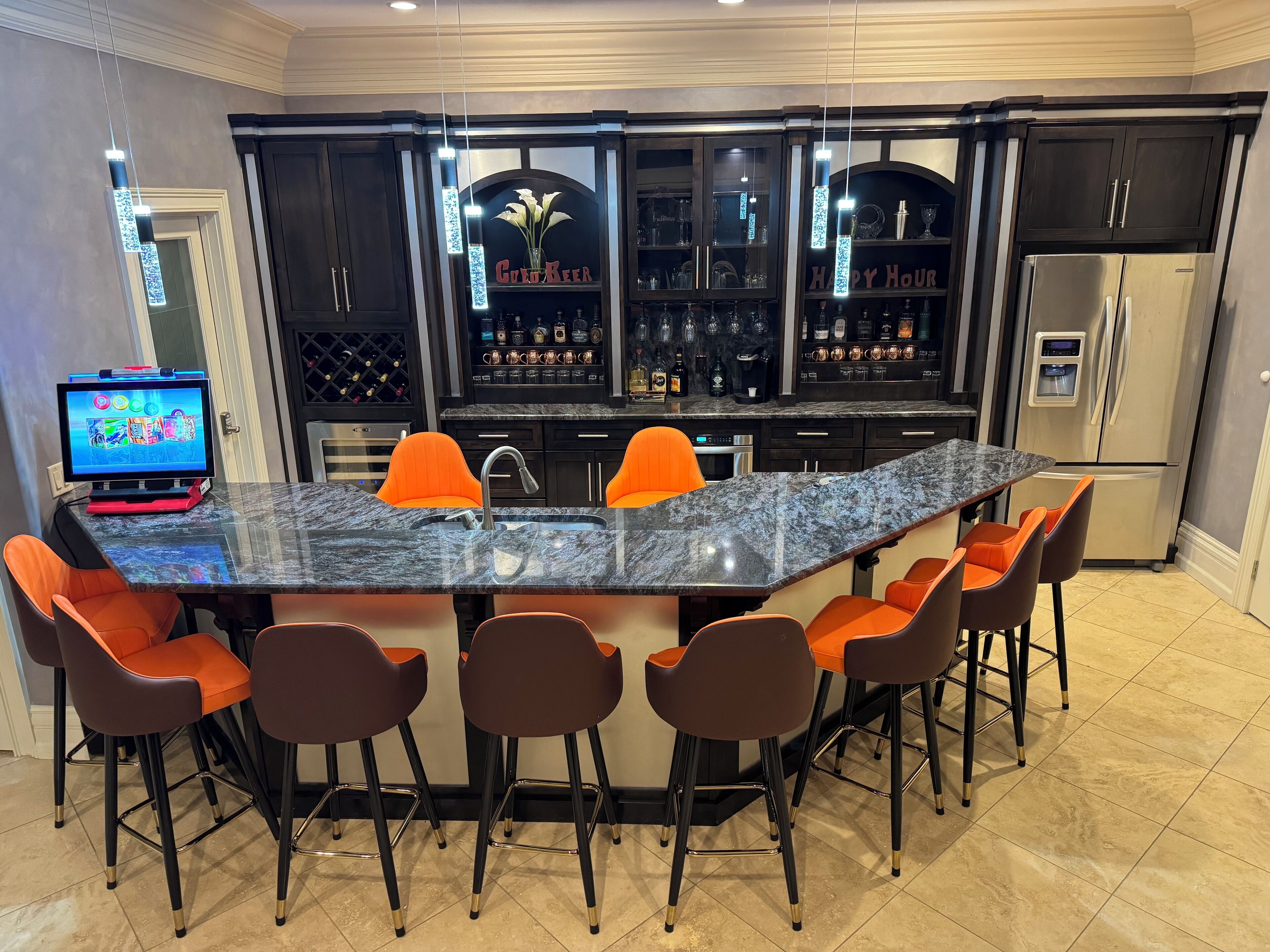 A modern kitchen with a bar area, featuring a granite countertop, bar stools, and a refrigerator.