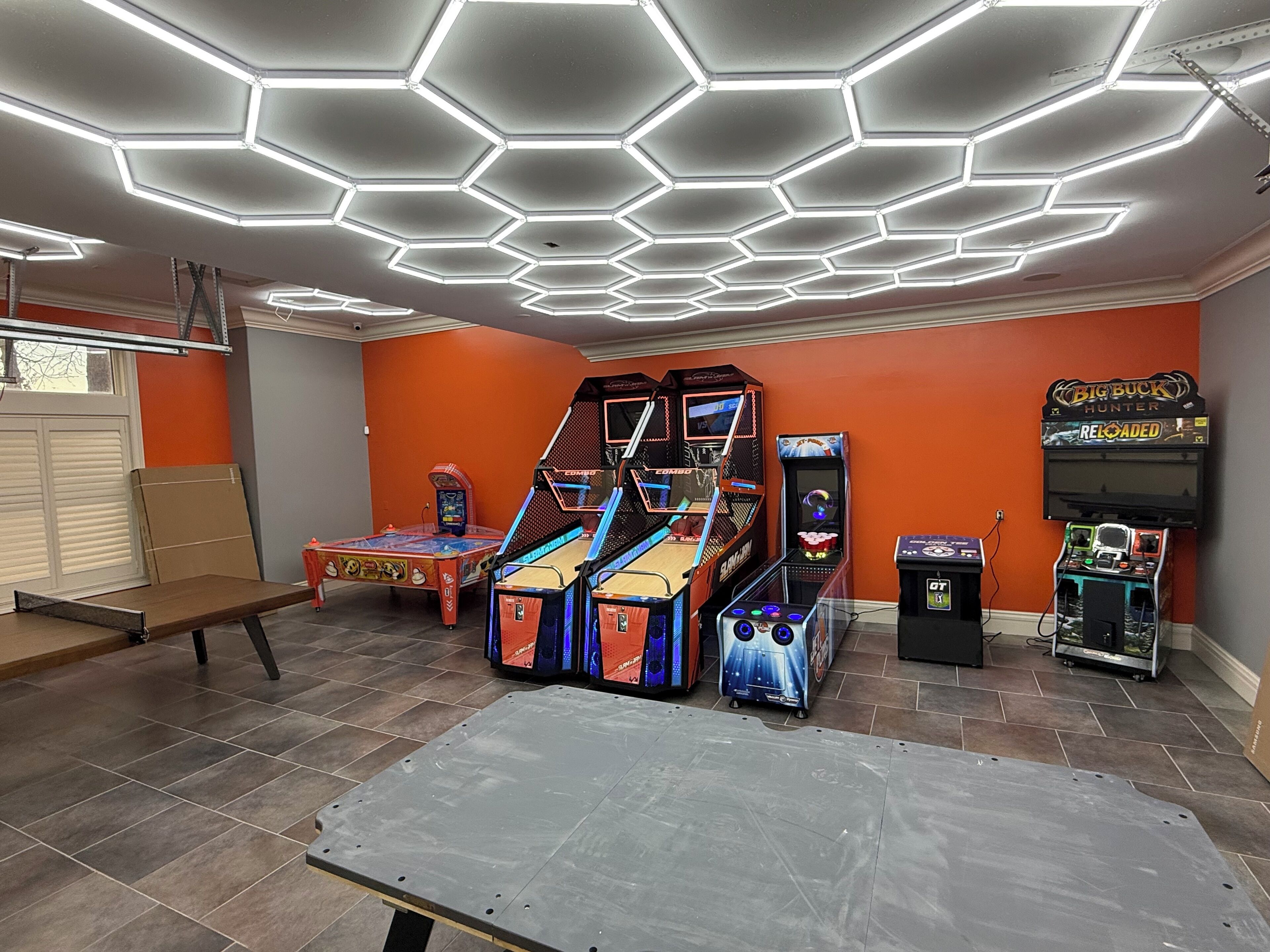 Una habitació amb llums de sostre hexagonals, jocs d'arcade i una taula.
