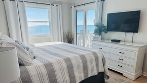 Ein Schlafzimmer mit einem Bett, einem Fernseher, einer Kommode und Blick auf das Meer.