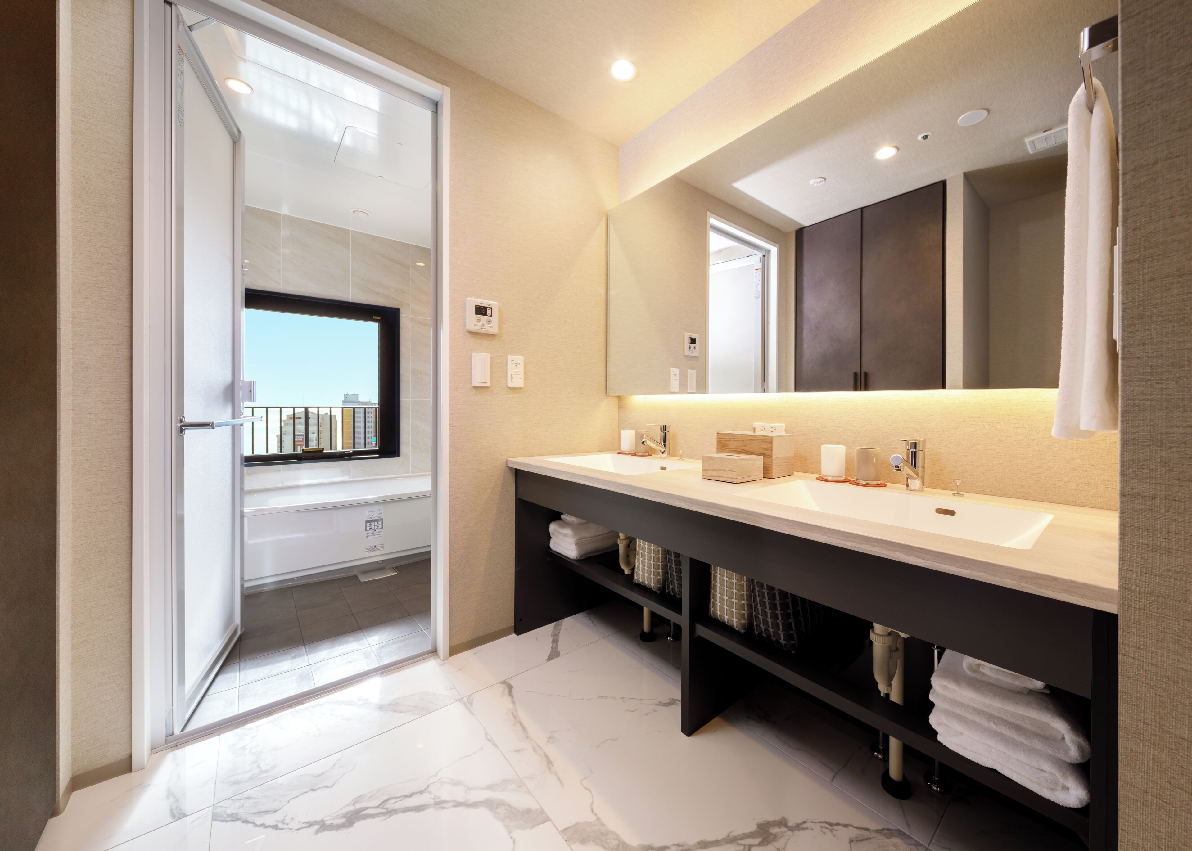 A modern bathroom with a large mirror, two sinks, a shower area, and a view through a glass door.
