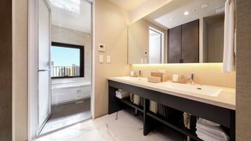 A modern bathroom with a large mirror, two sinks, a shower area, and a view through a glass door.