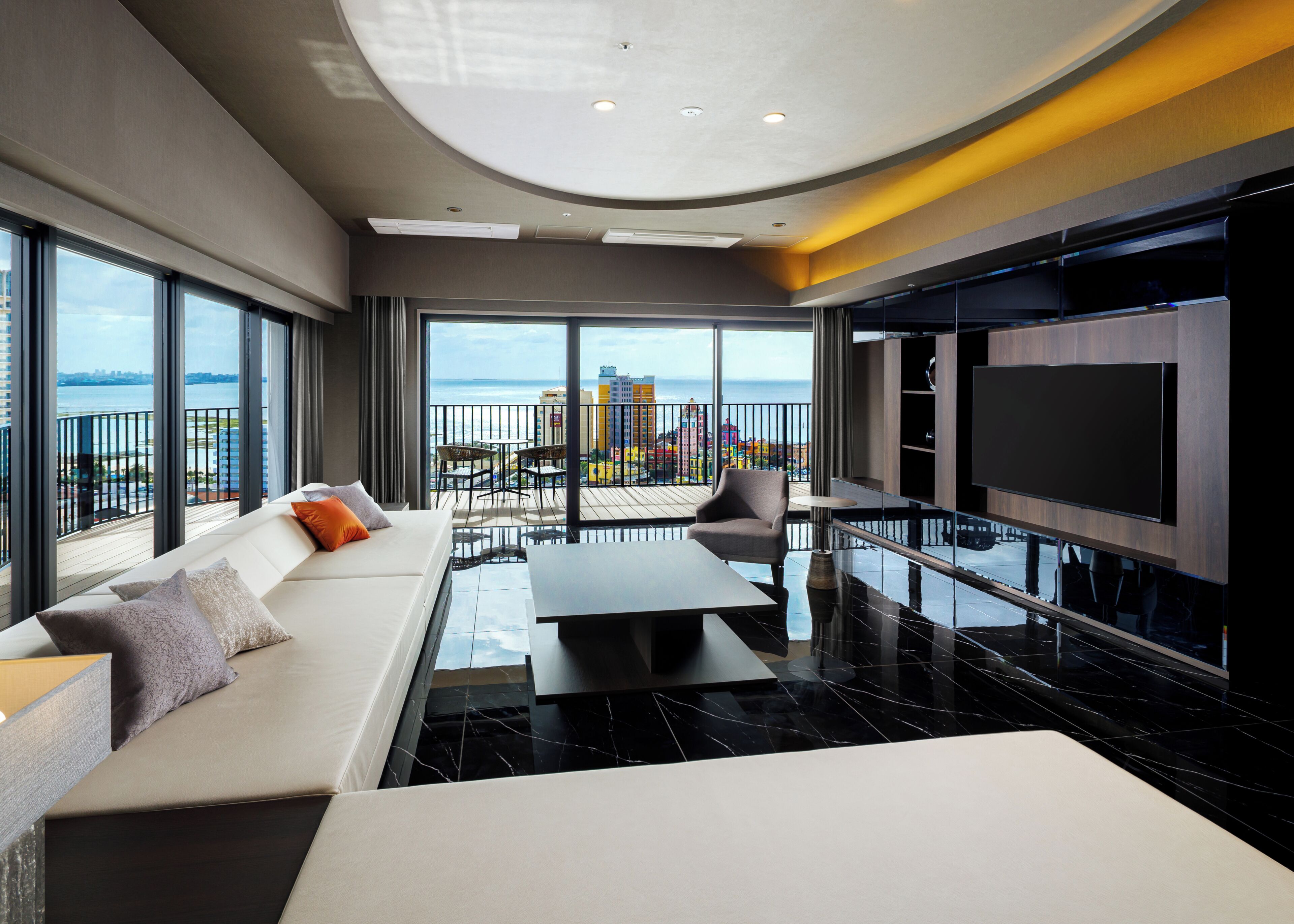 Quarto de hotel moderno com varanda, sofá, televisão e vista da cidade.
