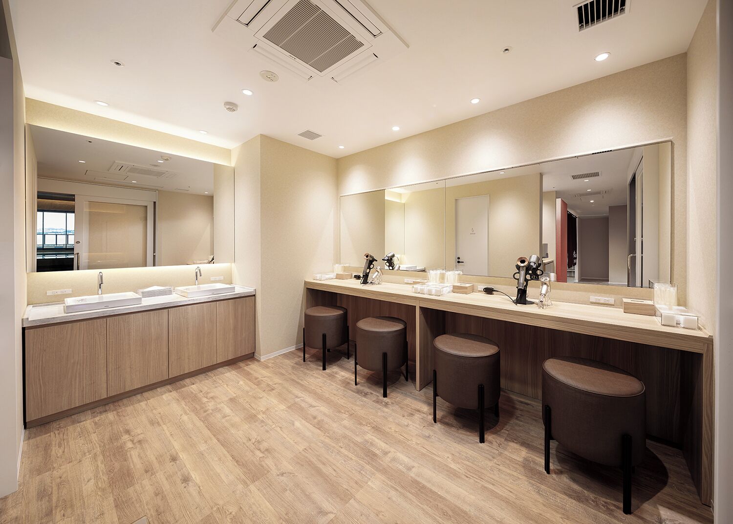 Un baño moderno con un espejo grande, varios lavamanos y taburetes.