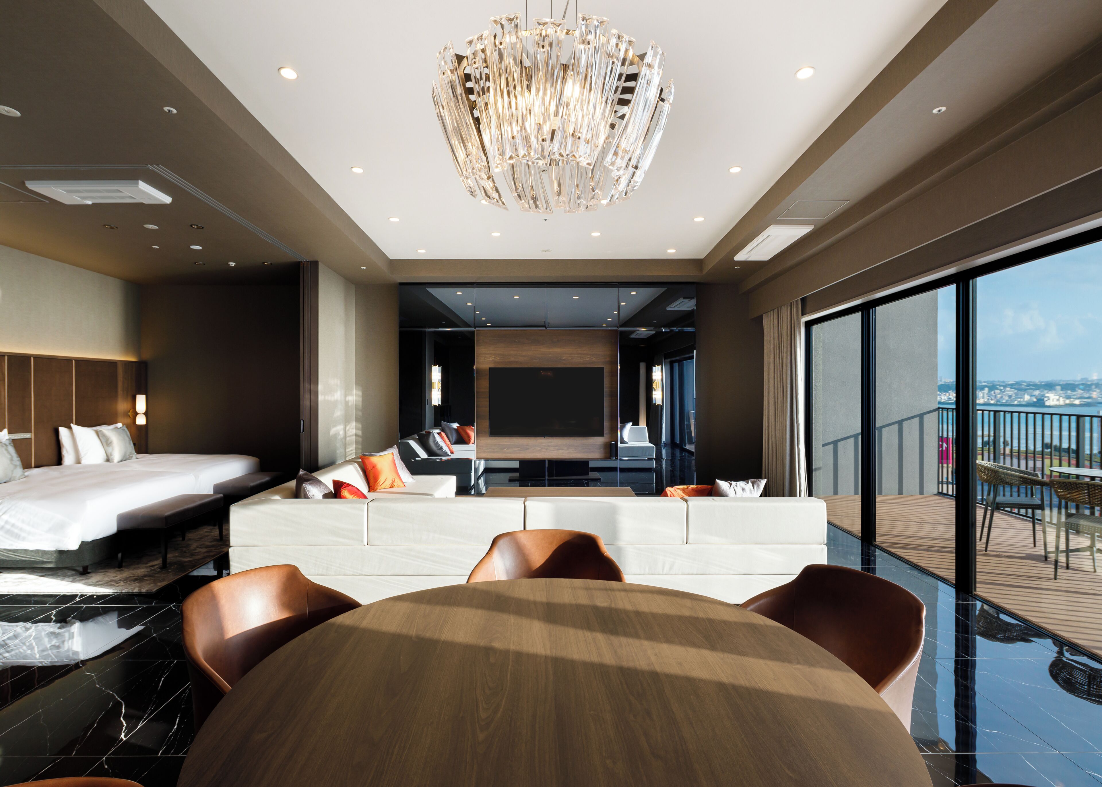 Quarto de hotel moderno com cama grande, área de estar, mesa de jantar e varanda com vista para a cidade.