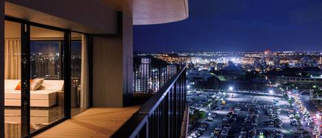 Un balcón con vistas a un paisaje urbano nocturno, un estacionamiento y un edificio de diseño moderno.