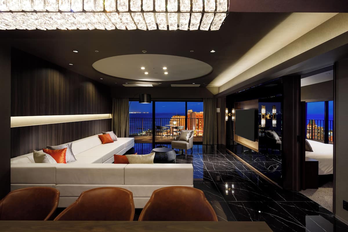 A modern hotel room with a balcony, a dining area, and a large TV screen.
