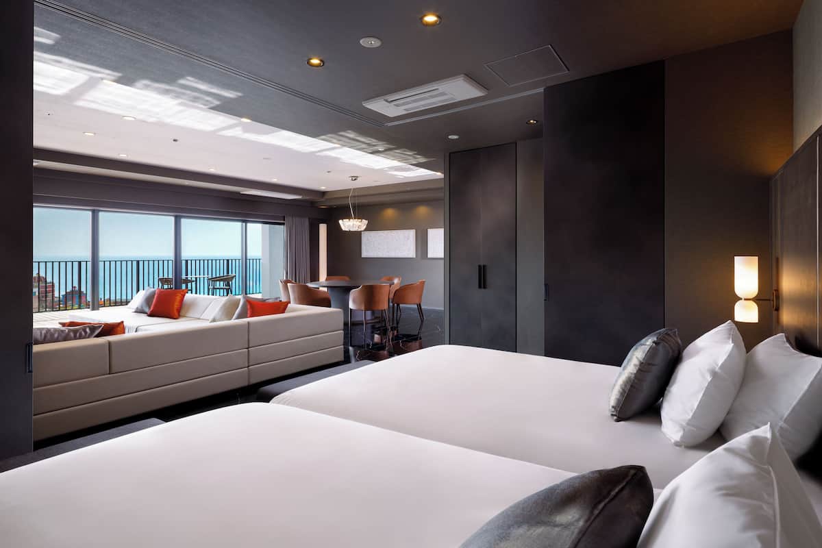 A modern hotel room with a large bed, a dining area, and a balcony with a view.