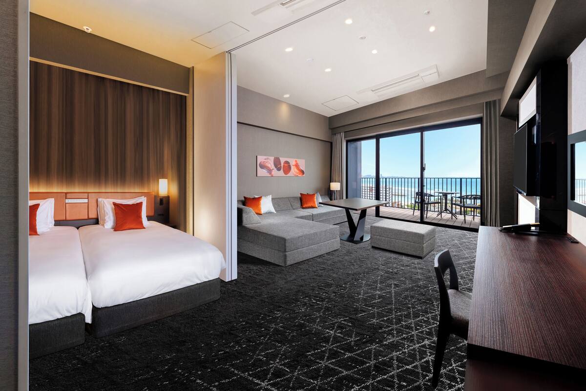 A hotel room with a large bed, a sofa, a dining table, and a TV.