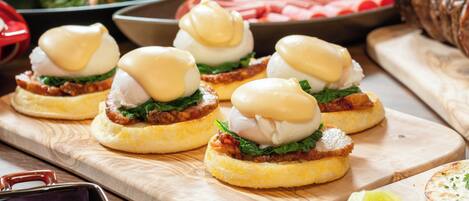 A wooden table with food items, including sandwiches with poached eggs and greens, and a bowl of sliced meat.