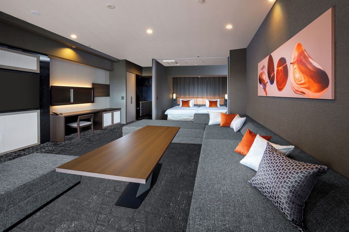 A modern hotel room with a large bed, a desk, and a seating area with a coffee table.