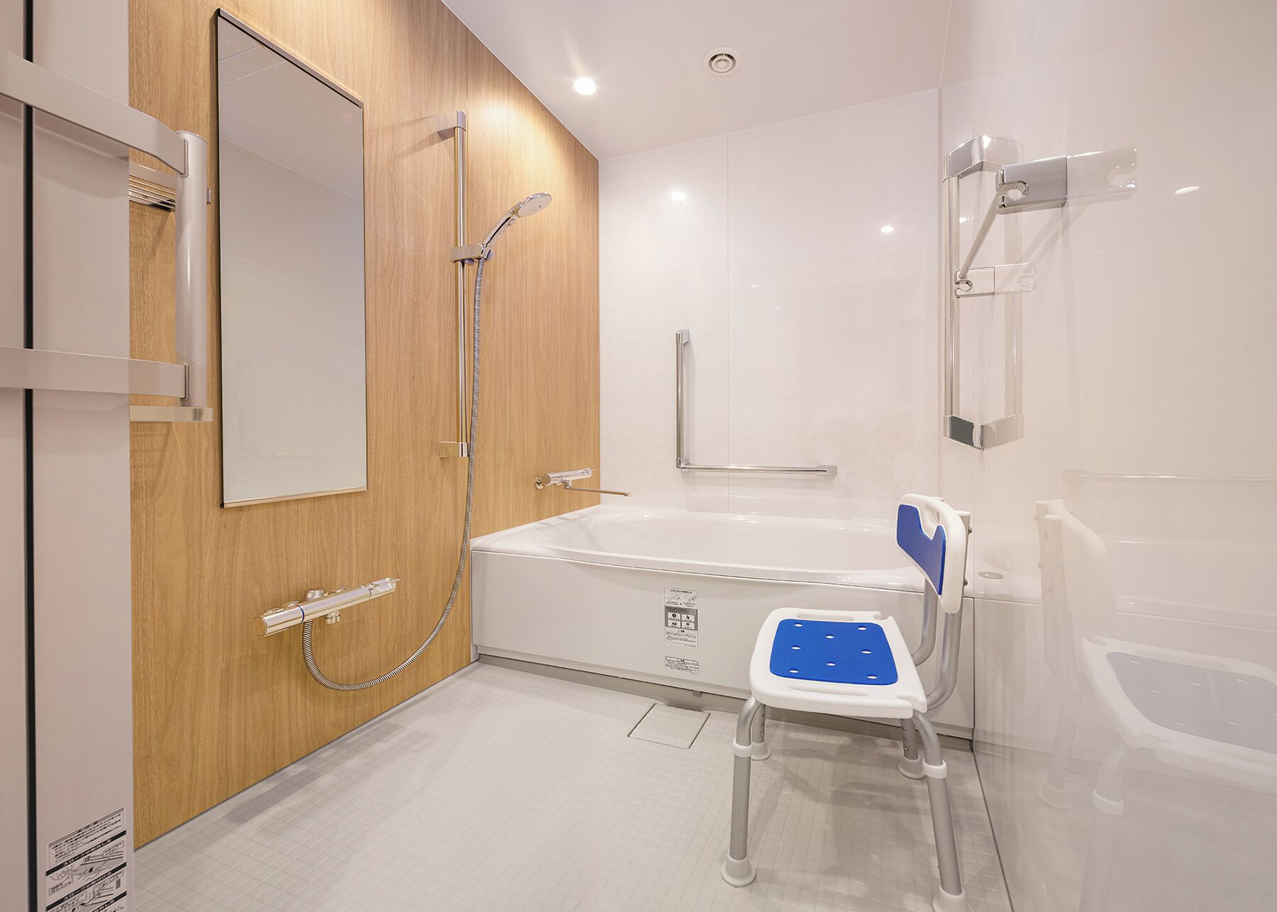 A modern bathroom with a wooden panel wall, a white bathtub, a shower with a handheld showerhead, and a blue and white step stool.
