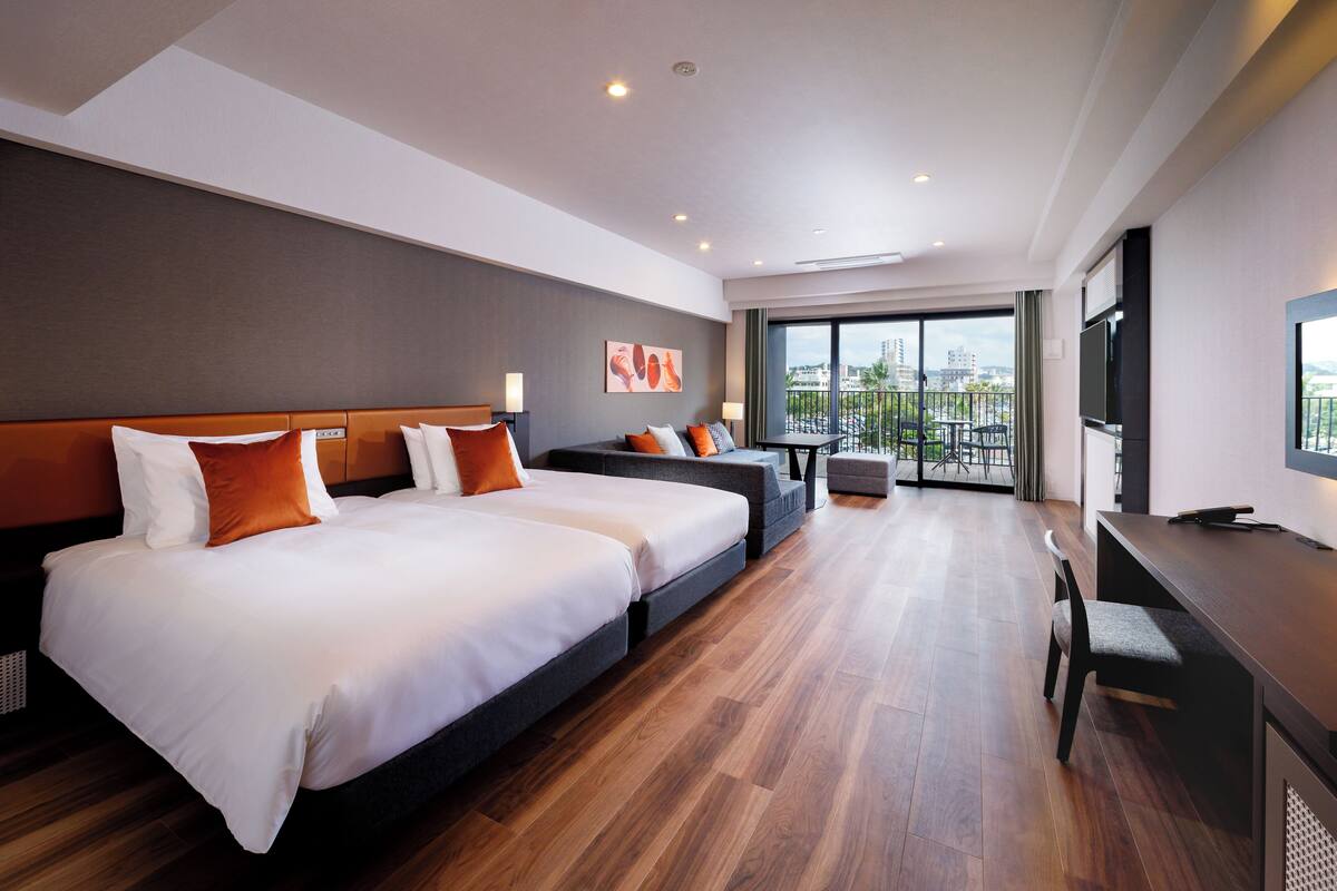 A hotel room with two beds, a balcony, a desk, and a TV.