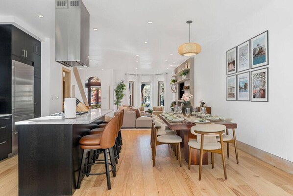 Cocina moderna con una isla central, comedor con sillas de madera y un amplio ventanal.