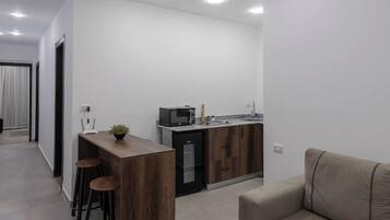 A modern kitchen with a microwave, sink, and wooden cabinets. There is a bar counter with stools and a plant.