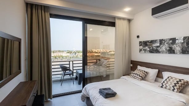 Una habitación de hotel moderna con una cama grande, un balcón con vistas y aire acondicionado.