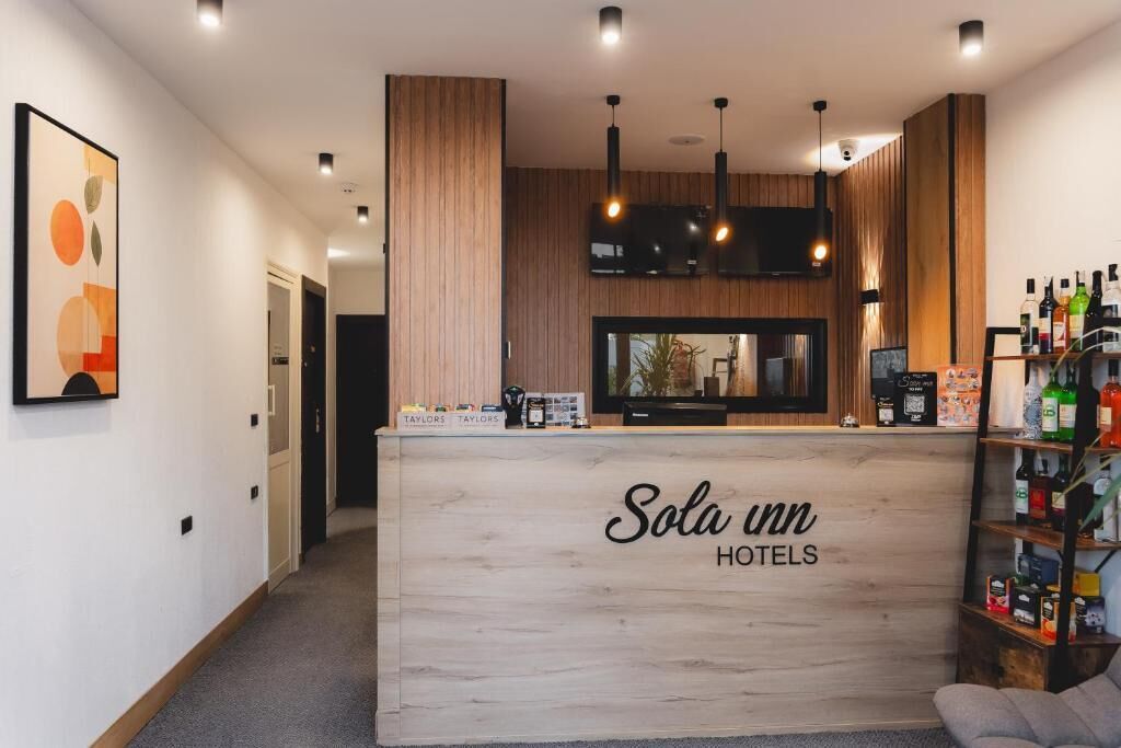 A reception desk at Sola inn with a wooden finish, a flat-screen TV, and a shelf with various items.