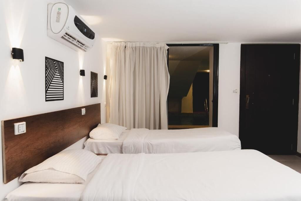 A hotel room with two single beds, a wall-mounted air conditioner, and a sliding door leading to a balcony.