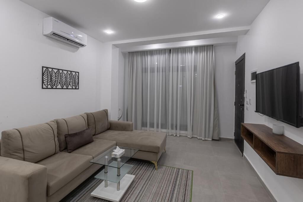 A modern living room with a beige sectional sofa, a glass coffee table, and a flat-screen TV mounted on the wall.