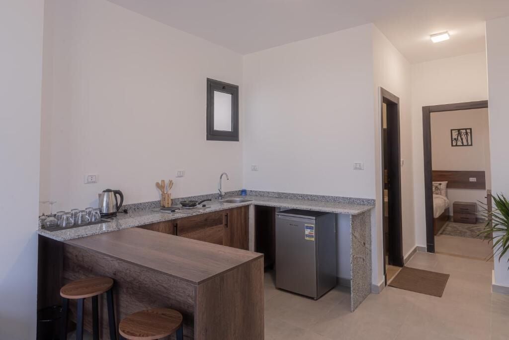 A compact kitchen with a granite countertop, a built-in dishwasher, and wooden stools.