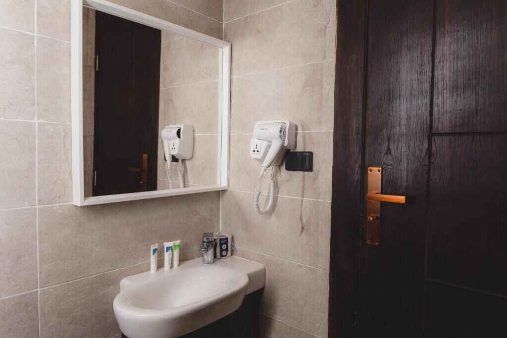 A bathroom with a white sink, a mirror, a hairdryer, and a door.