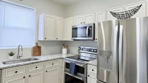 A modern kitchen with white cabinets, stainless steel appliances, a ceiling fan, and a clock on the wall. - 2BR Steps to Boardwalk & Beach, Walk to Casinos (Atlantic City)