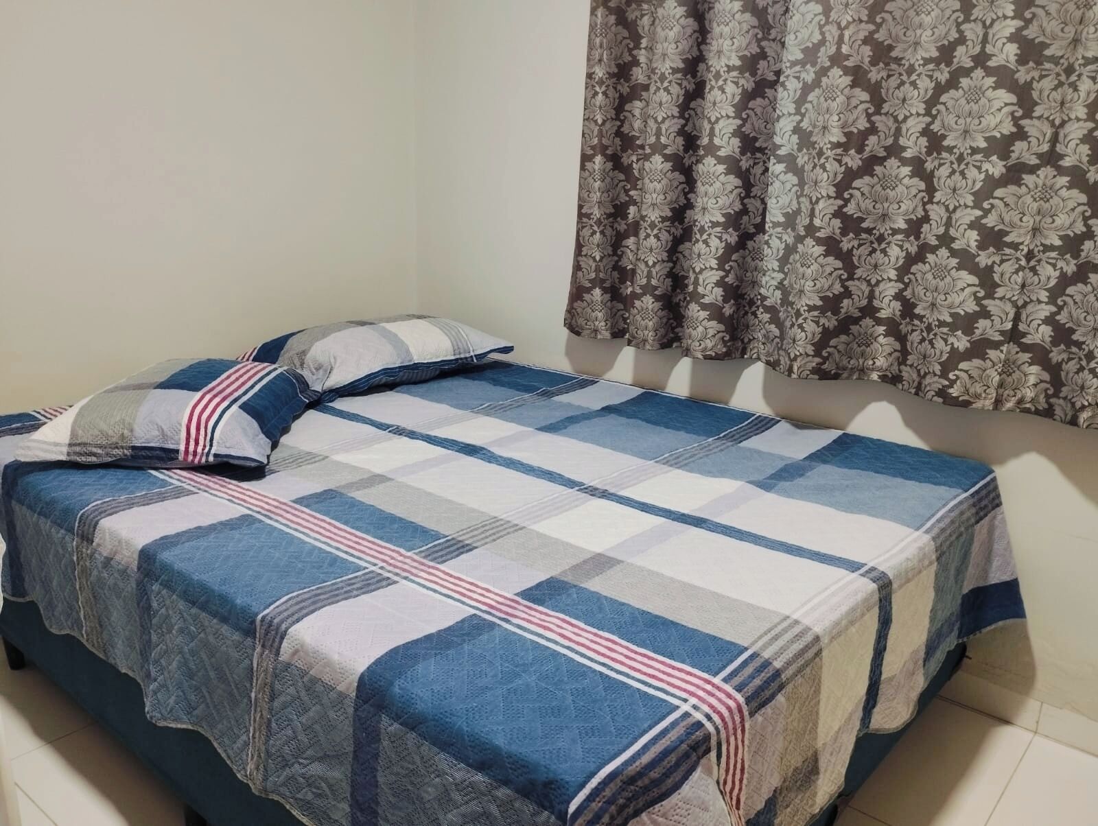 Una cama individual con colcha azul y blanca a cuadros y dos almohadas, una a rayas y otra lisa.