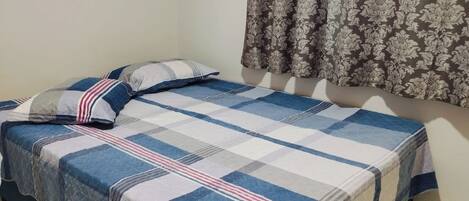 Una cama individual con colcha azul y blanca a cuadros y dos almohadas, una a rayas y otra lisa.