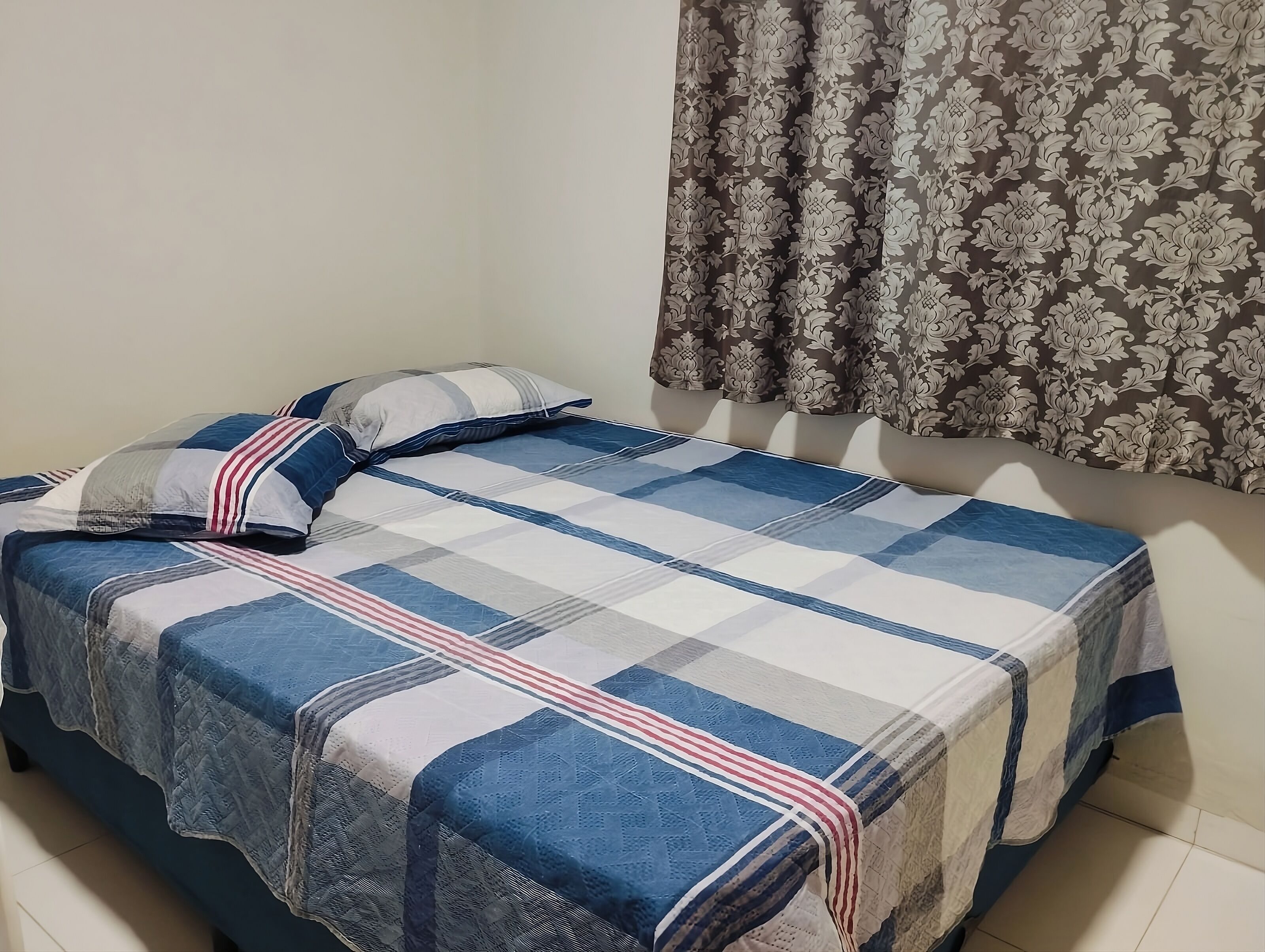 A bed with a checkered bedspread, two pillows, and a floral curtain.