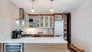 Una cucina moderna con un piano di lavoro bianco, mobili in legno, un piccolo frigorifero per il vino integrato e un forno a incasso.