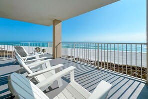 En balkon med hvide liggestole, udsigt til stranden og en klar blå himmel.