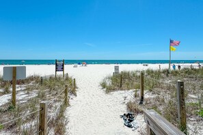 A sandy beach path leading to the ocean with a wooden fence and a flag. - Corner Beachfront Condo w/ Sunrise Balcony, Pools & Gulf Views | BEACHBALL PROPERTIES (Orange Beach)