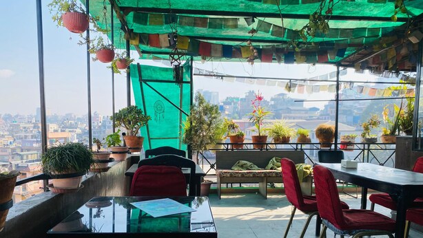 Een terras op het dak met uitzicht over de stad, voorzien van tafels, stoelen en potplanten.