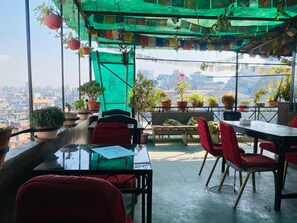 A rooftop terrace with a view of the city, furnished with tables, chairs, and potted plants. - Three Peaks Inn (Kathmandu)