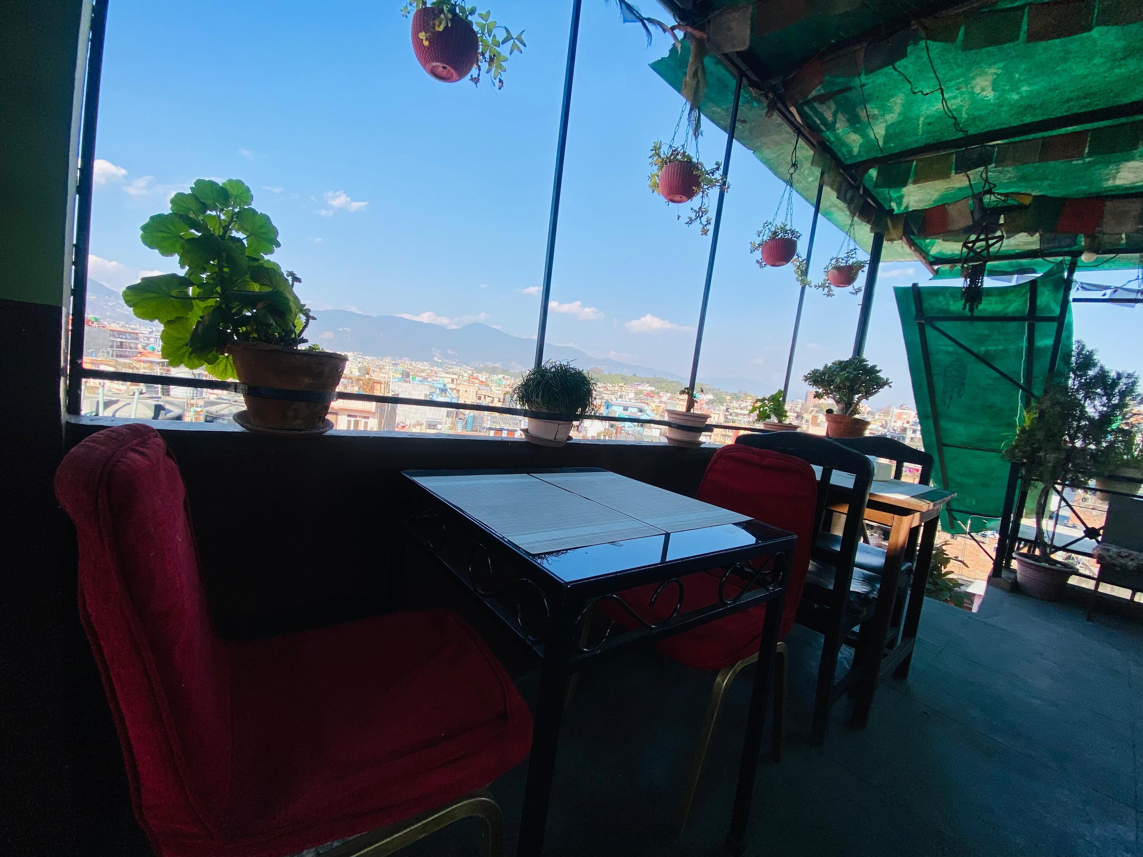 A balcony with a table and chairs, potted plants, and a view of a cityscape with mountains.