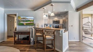 A modern kitchen with a central island, bar stools, a flat-screen TV, and a hanging chair.