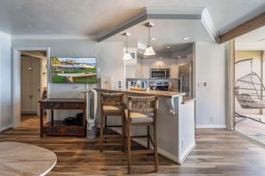 A modern kitchen with a central island, bar stools, a flat-screen TV, and a hanging chair.