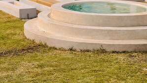 A modern outdoor pool area with a lounge chair, steps leading to the pool, and a view of a hill with buildings in the background. - Glamor Kintamani (Kintamani)