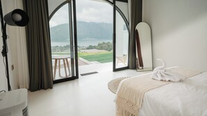 A bedroom with a bed, a mirror, and a view of a lake and mountains through a glass door. - Glamor Kintamani (Kintamani)
