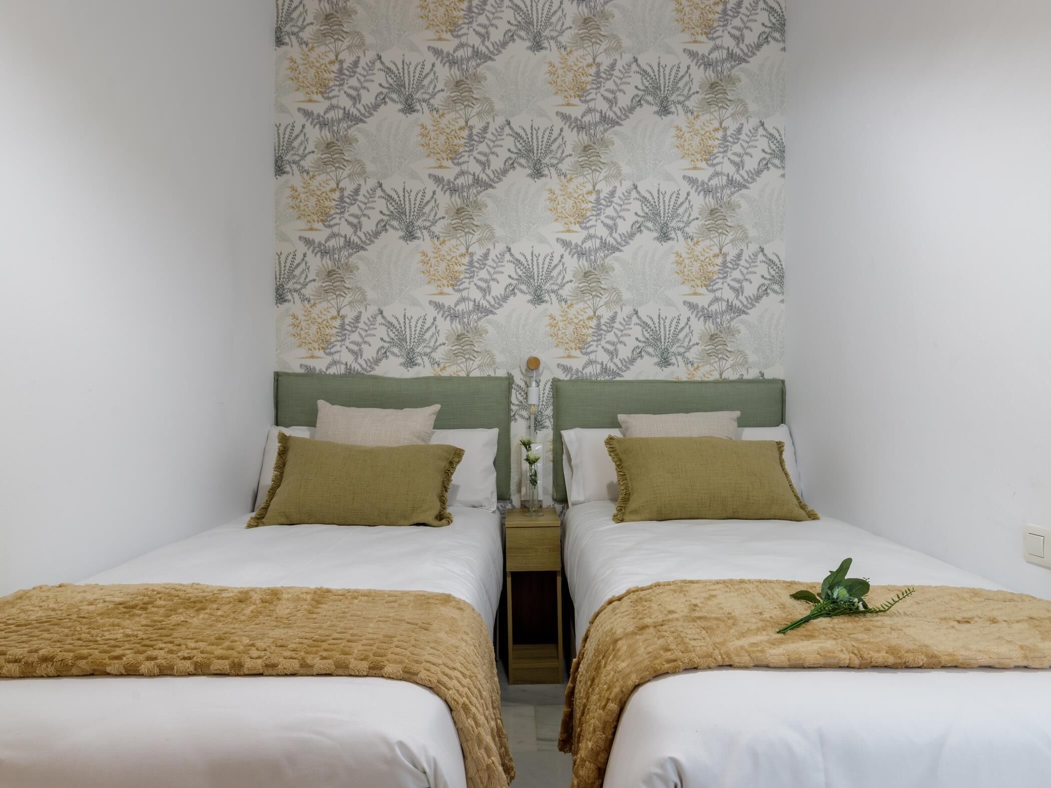 A room with two beds, each with a green headboard, white bedding, and a beige throw blanket.