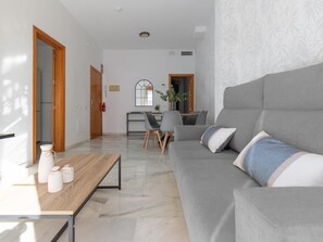 A modern living room with a grey sofa, a wooden coffee table, and a dining area with chairs and a table. - Urban Chic 3B - 2 dorm. Living4malaga (Distrito Centro)