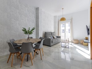 A modern living room with a dining area, featuring a sofa, chairs, a coffee table, and a vase with plants. - Urban Chic 3B - 2 dorm. Living4malaga (Distrito Centro)
