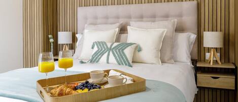 A neatly made bed with pillows, a bedside table with a lamp, and a tray with breakfast items.